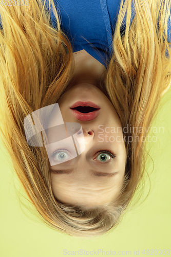 Image of Inverted portrait of caucasian young woman on yellow studio background