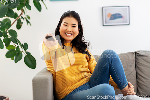 Image of asian woman with tv remote sitting on sofa at home