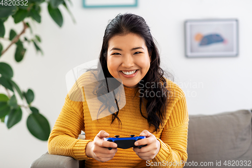 Image of asian woman with gamepad playing game at home