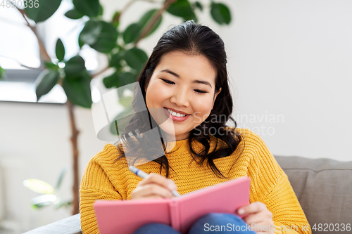 Image of asian woman with diary sitting on sofa at home