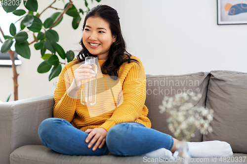 Image of smiling asian young woman drinking water at home