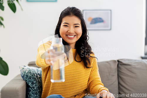 Image of smiling asian young woman drinking water at home