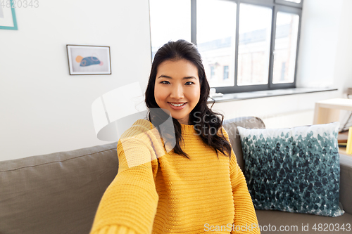 Image of smiling asian young woman taking selfie at home