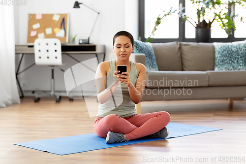 Image of woman with smartphone sits on exercise mat at home