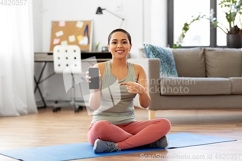 Image of woman with smartphone sits on exercise mat at home