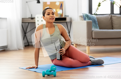 Image of smiling woman with bottle and dumbbells at home