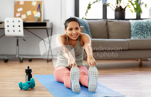 Image of african woman with earphones stretching at home
