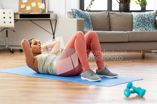 Image of african woman making abdominal exercises at home