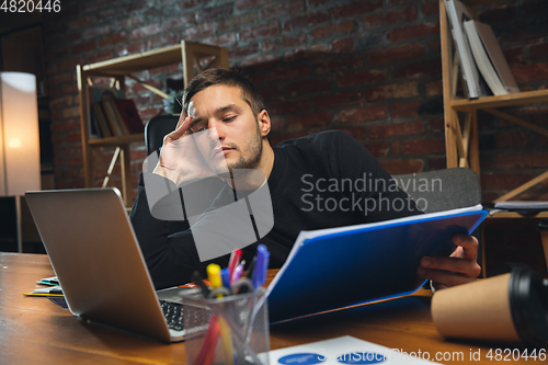 Image of Young man working in modern office using devices and gadgets. Making reports, analitycs, routine processing tasks