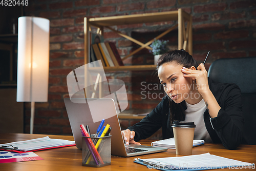 Image of Young woman working in modern office using devices and gadgets. Making reports, analitycs, routine processing tasks