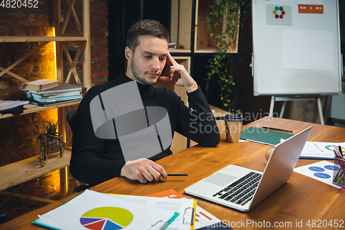 Image of Young man working in modern office using devices and gadgets. Making reports, analitycs, routine processing tasks