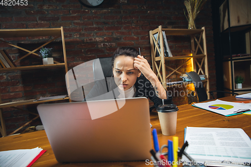 Image of Young woman working in modern office using devices and gadgets. Making reports, analitycs, routine processing tasks