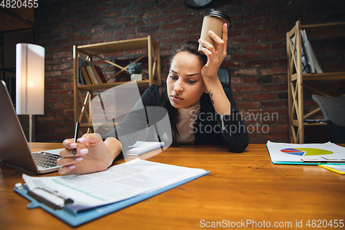 Image of Young woman working in modern office using devices and gadgets. Making reports, analitycs, routine processing tasks