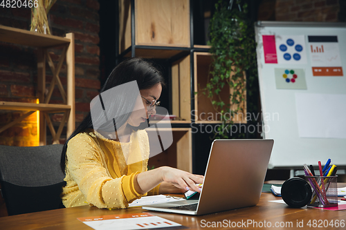 Image of Young woman working in modern office using devices and gadgets. Making reports, analitycs, routine processing tasks