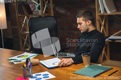 Image of Young man working in modern office using devices and gadgets. Making reports, analitycs, routine processing tasks