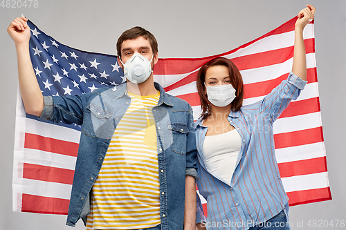 Image of couple in face masks holding flag of america