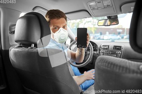 Image of male car driver in mask showing smartphone