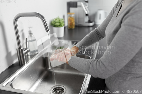 Image of woman washing hands with liquid soap in kitchen