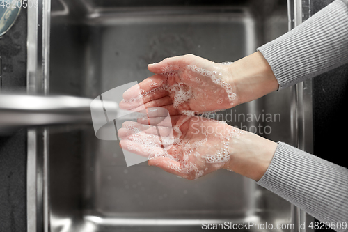 Image of woman washing hands with soap in kitchen