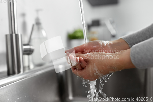 Image of woman washing hands with liquid soap in kitchen