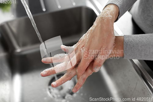 Image of woman washing hands with soap in kitchen