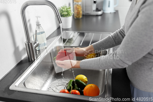 Image of woman washing fruits and vegetables in kitchen