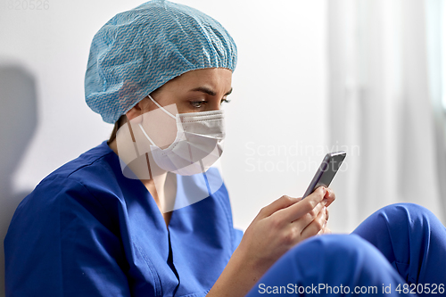 Image of sad doctor or nurse in face mask with smartphone