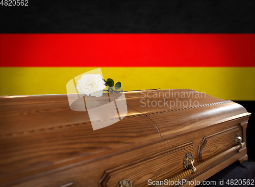 Image of white rose on wooden coffin over flag of germany