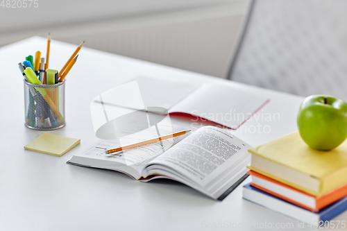 Image of books, apple and school supplies on table at home