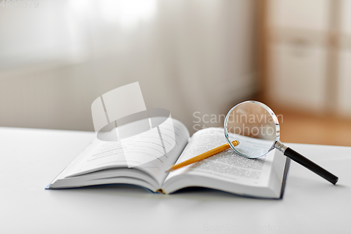 Image of book with magnifier and pencil on table at home