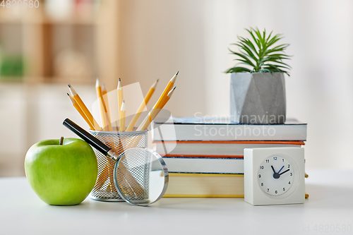 Image of books, magnifier, pencils, apple on table at home