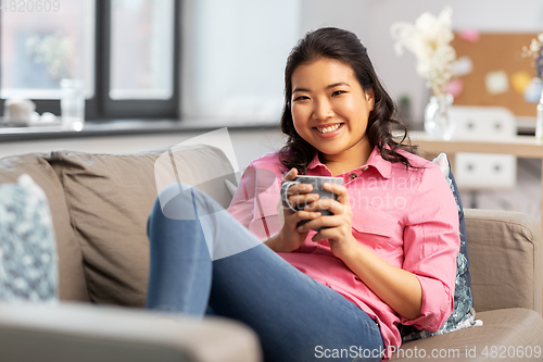 Image of smiling asian young woman drinking coffee at home