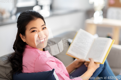 Image of smiling asian young woman reading book at home