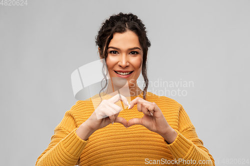 Image of smiling young woman making hand heart gesture