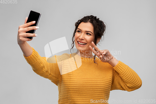 Image of smiling young woman taking selfie by smartphone