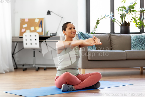 Image of african american woman stretching arm at home