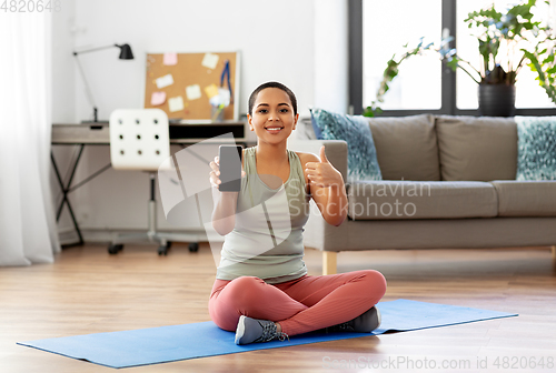 Image of woman with smartphone sits on exercise mat at home