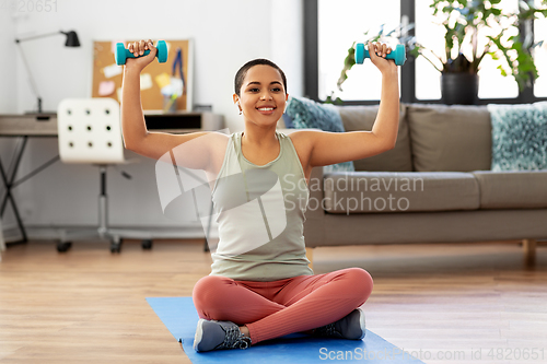 Image of african woman with dumbbells exercising at home