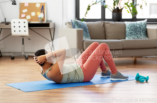 Image of african woman doing abdominal exercises at home