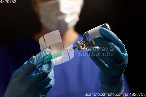 Image of doctor in face mask with syringe and medicine