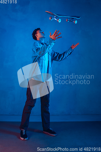 Image of Caucasian young skateboarder posing on dark neon lighted background