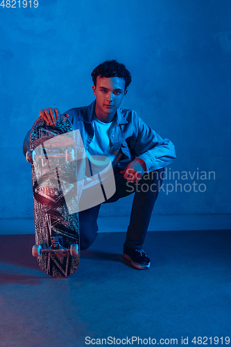 Image of Caucasian young skateboarder posing on dark neon lighted background