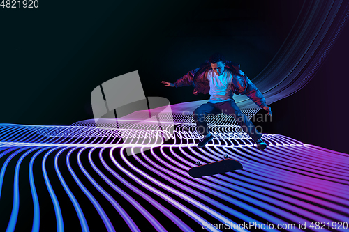 Image of Caucasian young skateboarder riding on dark neon lighted line background