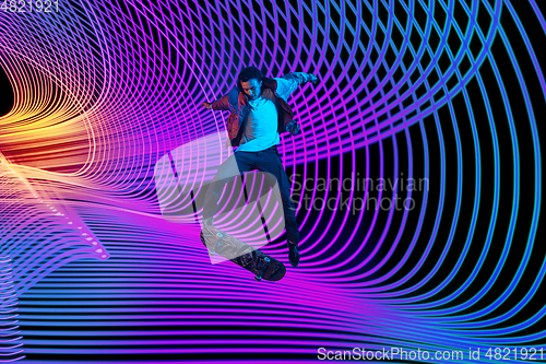 Image of Caucasian young skateboarder riding on dark neon lighted line background