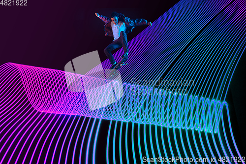 Image of Caucasian young skateboarder riding on dark neon lighted line background