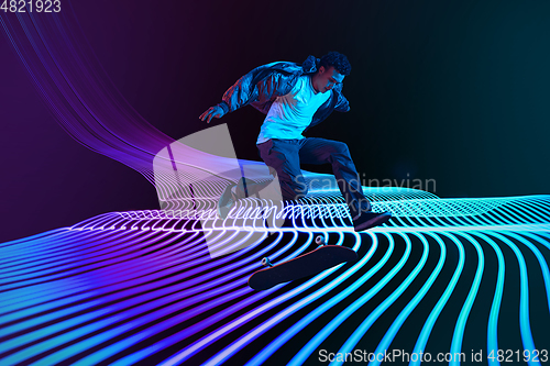 Image of Caucasian young skateboarder riding on dark neon lighted line background