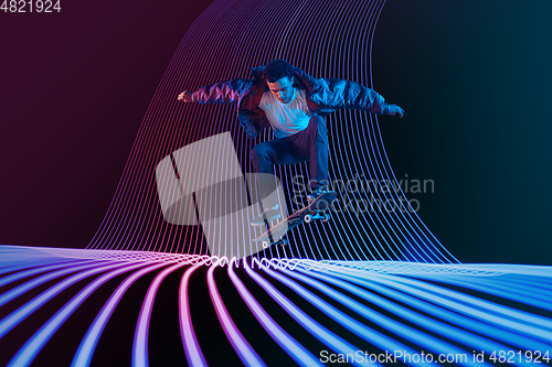 Image of Caucasian young skateboarder riding on dark neon lighted line background