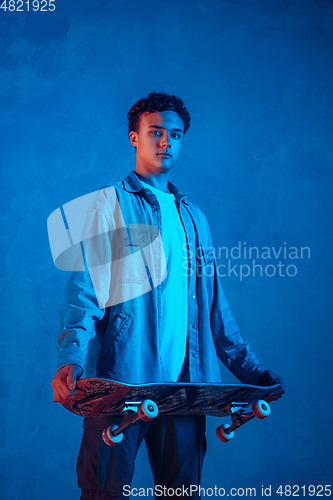 Image of Caucasian young skateboarder posing on dark neon lighted background