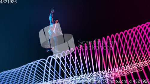 Image of Caucasian young skateboarder riding on dark neon lighted line background