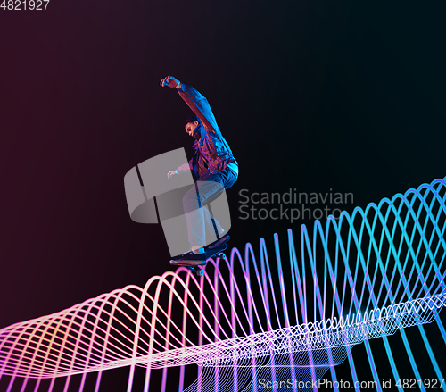 Image of Caucasian young skateboarder riding on dark neon lighted line background